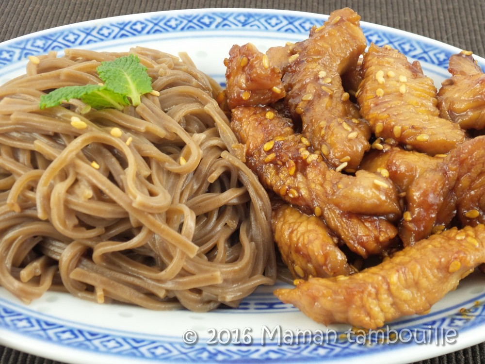 Assiette asiatique avec des nouilles soba accompagnées de morceaux de poulet caramélisé au miel, parsemés de graines de sésame."