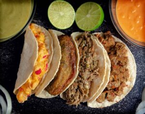 Tacos al pastor garnis de coriandre et d’oignon, servis avec une sauce rouge sur une assiette en céramique